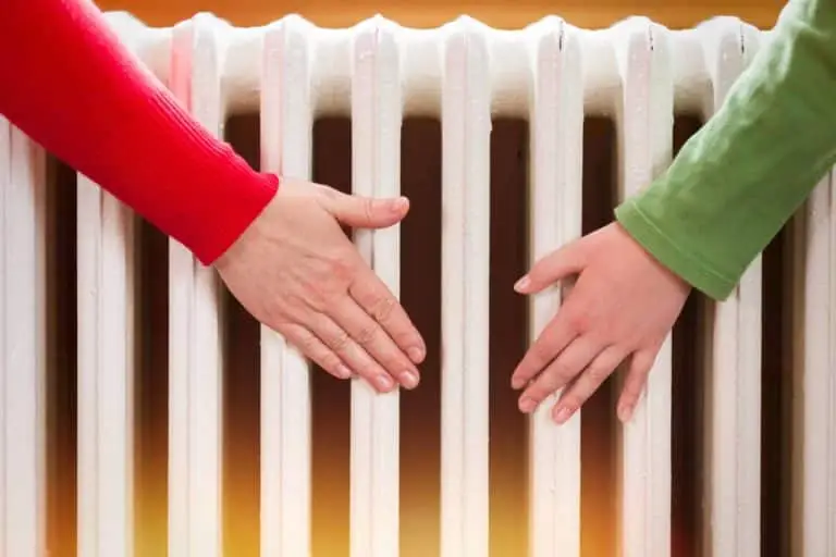 Two people warming their hands on a radiator to combat the cold.