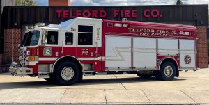 A red and white fire truck labeled "Telford Fire Co. Fire Rescue" is parked outside a brick fire station with "Telford Fire Co." written in large red letters above the garage door.
