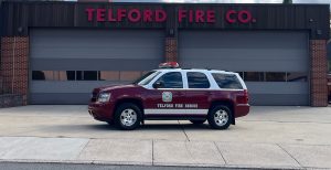 A red and white Telford Fire Rescue SUV is parked in front of a building with three closed garage doors, labeled "Telford Fire Co." in large red letters.