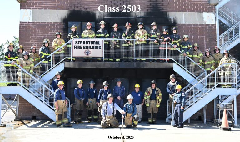 A large group of firefighters in full gear pose on and around a stairway outside a "Structural Fire Building." The sign above reads "Class 2503." The date "October 4, 2025" appears at the bottom of the image.